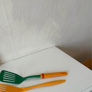 Peut inclure: Une spatule verte et orange et une fourchette jaune. Les deux ustensiles de cuisine sont en plastique.