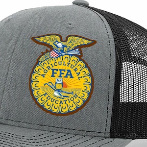 May include: A gray and black trucker hat featuring the FFA emblem. The emblem is a circular design with a yellow background, a blue owl, and the words "AGRICULTURAL EDUCATION" and "FFA". An eagle is at the top of the emblem.