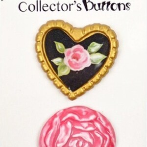 May include: Two decorative buttons featuring a pink rose design. The first button is a heart-shaped button with a gold frame and a black background. The second button is a round button with a pink rose design.