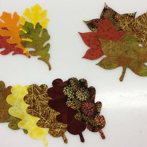 May include: A collection of fabric leaf cutouts in various autumn colors. The leaves feature patterns like floral prints and textured designs, with shades of red, orange, yellow, and brown. These decorative leaves are ideal for fall-themed crafts.