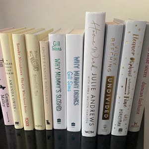 May include: A bookshelf displaying a collection of books in a variety of colours, including white, cream, and pink. The books have titles such as "Why Mummy Drinks", "Undivided", "Our Little Secret", and "Eleanor Oliphant is Completely Fine".
