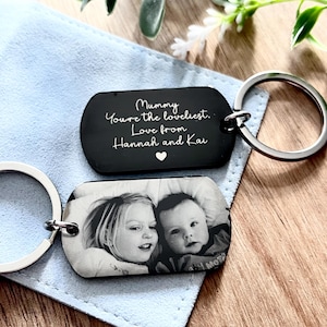 May include: Two rectangular metal keychains with silver-toned rings. One keychain features a black surface with white engraved text reading: Mummy You're the loveliest. Love from Hannah and Kai, with a small heart. The other shows a black and white photo.