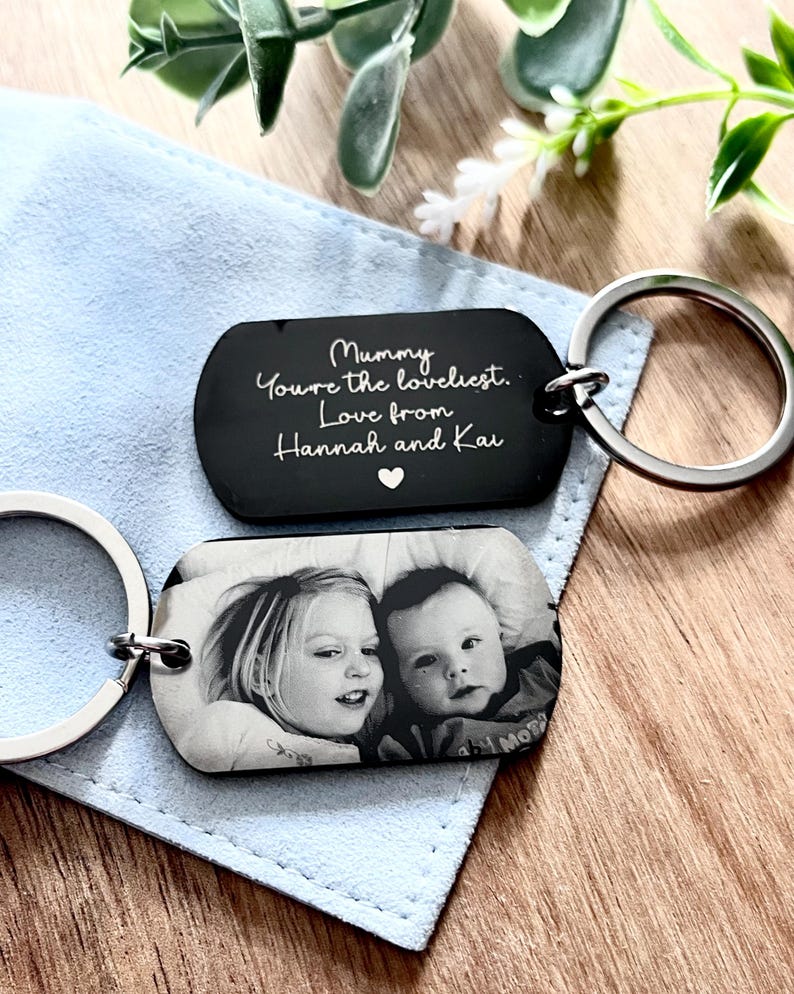May include: Two rectangular metal keychains with silver-toned rings. One keychain features a black surface with white engraved text reading: Mummy You're the loveliest. Love from Hannah and Kai, with a small heart. The other shows a black and white photo.