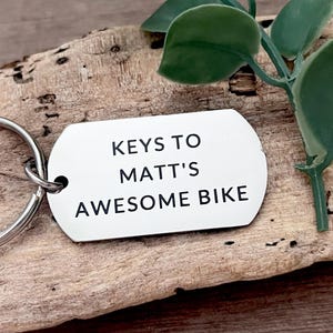 Peut inclure: Porte-clés en argent avec le texte "Keys to Matt's Awesome Bike" gravé dessus.