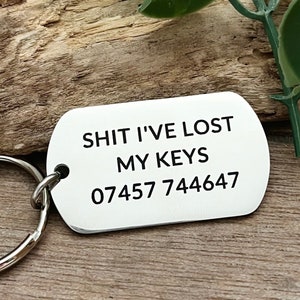 Può includere: Portachiavi d'argento con un'etichetta d'argento su cui è scritto "SHIT I'VE LOST MY KEYS 07457 744647"