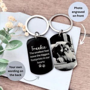 May include: Two silver-toned metal dog tag keychains with circular rings. One tag features a black surface with the engraved text Frankie, The smallest feet leave the biggest footprints in our hearts, and two paw prints. The other tag shows a photo.