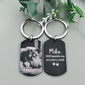 May include: Two black metal dog tag keychains with silver split rings. One tag features a laser-engraved black and white photograph of a dog. The other tag displays the white text Mika, Still beside me on every walk, and two paw print icons.