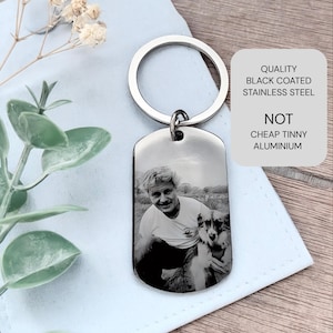 May include: A silver-toned metal dog tag keychain featuring a laser-engraved black and white photograph of a person and a dog. The text on the image reads: QUALITY BLACK COATED STAINLESS STEEL NOT CHEAP TINNY ALUMINIUM. The tag has a round ring.