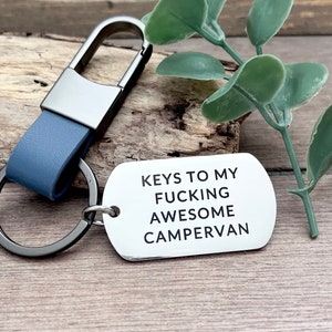 May include: A silver metal keychain with a blue leather strap and a tag that reads "KEYS TO MY FUCKING AWESOME CAMPERVAN".