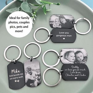 May include: A collection of rectangular metal keychains with rounded corners, featuring engraved black-and-white photographs and personalized text. The keychains include silver-toned split rings and display various inscriptions like Mika, Love you gorgeous man, and Daddy we love you so much.
