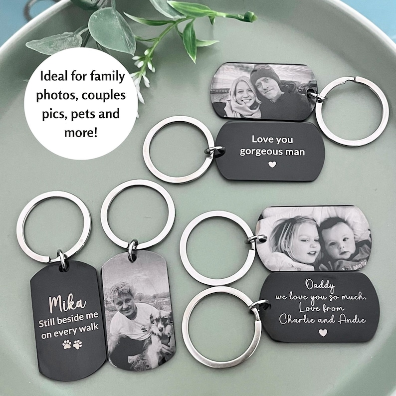 May include: A collection of rectangular metal keychains with rounded corners, featuring engraved black-and-white photographs and personalized text. The keychains include silver-toned split rings and display various inscriptions like Mika, Love you gorgeous man, and Daddy we love you so much.