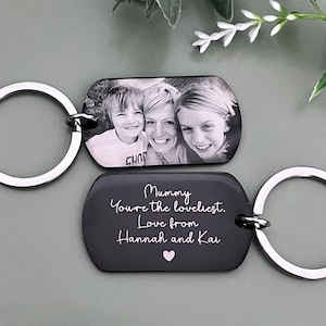 May include: Two rectangular metal keychains with rounded corners and silver-toned split rings. One keychain features a black and white photograph of three people. The other is black with white engraved text: Mummy You're the loveliest. Love from Hannah and Kai, and a small pink heart.