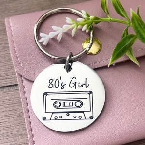 May include: A silver keychain with a round tag that says "80's Girl" and has a black and white illustration of a cassette tape.