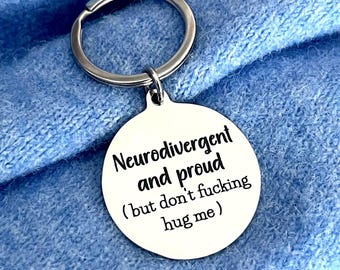 May include: A circular silver-toned metal keyring featuring a split ring and an engraved disc. The text on the disc reads: Neurodivergent and proud ( but don't fucking hug me ). The metal surface is smooth and reflective with black lettering.