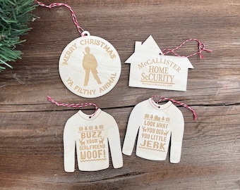 May include: Four wooden Christmas ornaments featuring Home Alone themes. The ornaments are shaped like a house, a sweater, and two circles. The house ornament says "McCallister Home Security Founded Chicago IL 1990". One circle ornament says "Merry Christmas Ya Filthy Animal" with a silhouette of Kevin McCallister. The other circle ornament says "Buzz Your Girlfriend Woof!" with a reindeer and Christmas tree design. The sweater ornament says "Look What You Did You Little Jerk" with a Christmas tree design.