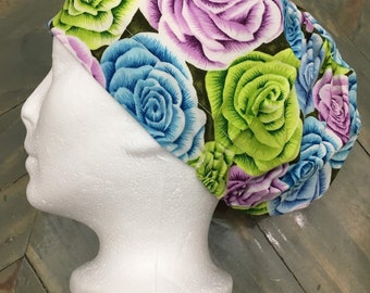 May include: A colorful floral print scrub hat with green, blue, and purple roses on a dark background.