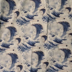 May include: A fabric pattern featuring a repeating design of white sharks with dark blue eyes and open mouths, integrated into stylised dark blue ocean waves with white foam crests against a light cream-coloured background.