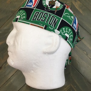 May include: A green, black, and white Boston Celtics scrub cap. The cap features the team's logo, the NBA logo, and the word "BOSTON" in large green letters. The cap is on a white mannequin head.
