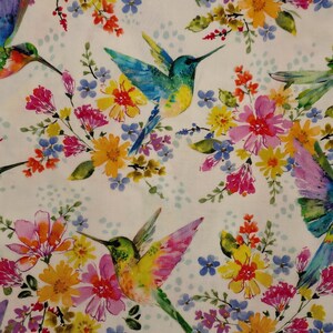 May include: A white fabric featuring a repeating pattern of colorful hummingbirds in shades of blue, green, and pink, interspersed with clusters of yellow, pink, and blue wildflowers and small light blue dots across the surface.