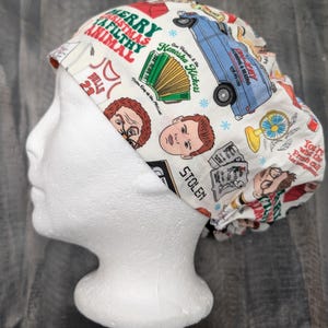 May include: A white scrub hat with a Christmas Vacation themed print. The print features characters from the movie, including Clark Griswold, Cousin Eddie, and the family dog. The text on the hat reads "Merry Christmas Ya Filthy Animal".