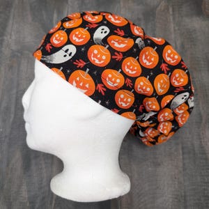 Może przedstawiać: Czarny czepek chirurgiczny z nadrukiem o tematyce Halloween z pomarańczowymi dyniami i białymi duchami. Czepek wykonany jest z miękkiej, wygodnej tkaniny i idealnie nadaje się dla pielęgniarek, lekarzy i innych pracowników służby zdrowia.