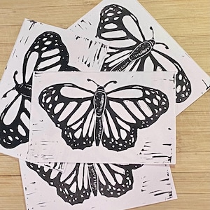 May include: Four black and white linocut prints of butterflies. Each print features a butterfly with detailed wings and a simple body.