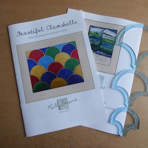 May include: A quilting pattern booklet titled "Beautiful Clamshells" with instructions on how to prepare and piece them. The booklet features a colourful clamshell design with red, blue, green, and yellow fabric. The booklet is accompanied by four clear plastic clamshell templates.