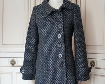 May include: A grey and blue patterned coat with a classic design. The coat features a collared neckline, button-down closure, and long sleeves with buttoned cuffs. It is displayed on a wooden mannequin stand.
