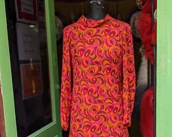 May include: A vintage dress with a geometric pattern in shades of orange, pink, and brown. The dress has a high neck and long sleeves.