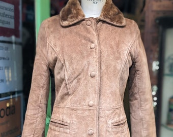 Puede incluir: Una chaqueta de ante marrón con cuello y puños de piel sintética. La chaqueta tiene cierre de botones y dos bolsillos.