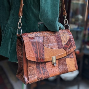 Peut inclure: Un sac à main en cuir marron avec un design patchwork de différents imprimés animaliers. Le sac a une longue bandoulière marron et un fermoir argenté.