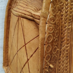 Puede incluir: Un bolso de cuero marr&oacute;n con intrincados detalles en relieve y costuras. El bolso tiene una forma rectangular y un cierre de solapa.