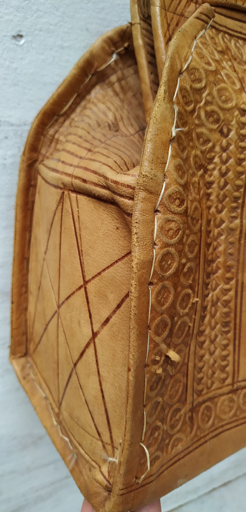 Puede incluir: Un bolso de cuero marr&oacute;n con intrincados detalles en relieve y costuras. El bolso tiene una forma rectangular y un cierre de solapa.