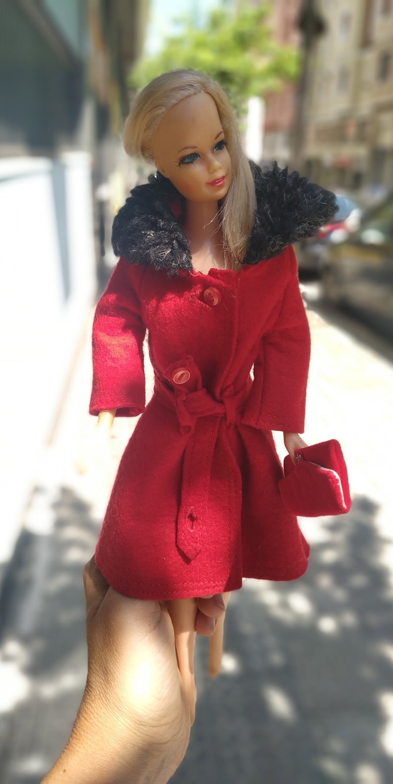 May include: A red coat with a black fur collar and a small red purse. The coat has a belt and buttons.