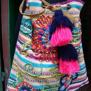 May include: A colorful striped fabric bag with beaded embroidery and pink and blue tassels. The bag has a drawstring closure and a leather strap.