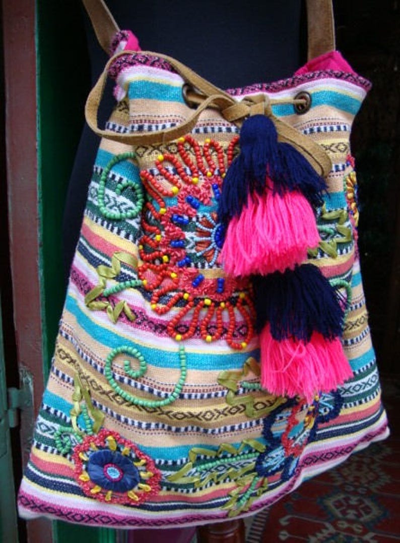 May include: A colorful striped fabric bag with beaded embroidery and pink and blue tassels. The bag has a drawstring closure and a leather strap.