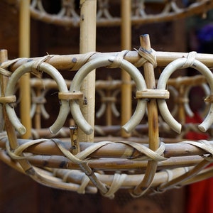 May include: A close-up of a woven bamboo lampshade with a circular shape and a natural brown color. The lampshade is made of thin, interwoven bamboo strips, creating a delicate and intricate pattern.