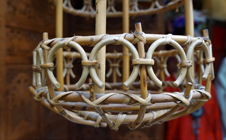 May include: A close-up of a woven bamboo lampshade with a circular shape and a natural brown color. The lampshade is made of thin, interwoven bamboo strips, creating a delicate and intricate pattern.