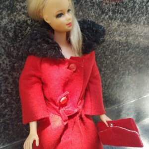 May include: A vintage doll wearing a red coat with a black fur collar and a red purse. The doll has blonde hair and blue eyes.