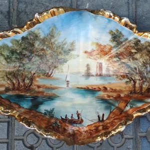 Może przedstawiać: Porcelanowa miska z pozłacanym brzegiem i malowanym obrazem rzeki z drzewami, żaglówką i zamkiem w oddali.