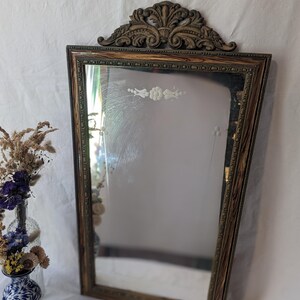 May include: A vintage wood framed mirror with a decorative carved top and etched floral design. The mirror has a distressed wood finish and a beveled edge.