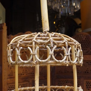 May include: A round, woven bamboo pendant light fixture with a natural brown color. The light fixture has a circular top and bottom with a woven design. The fixture is suspended from a single, thick bamboo pole.