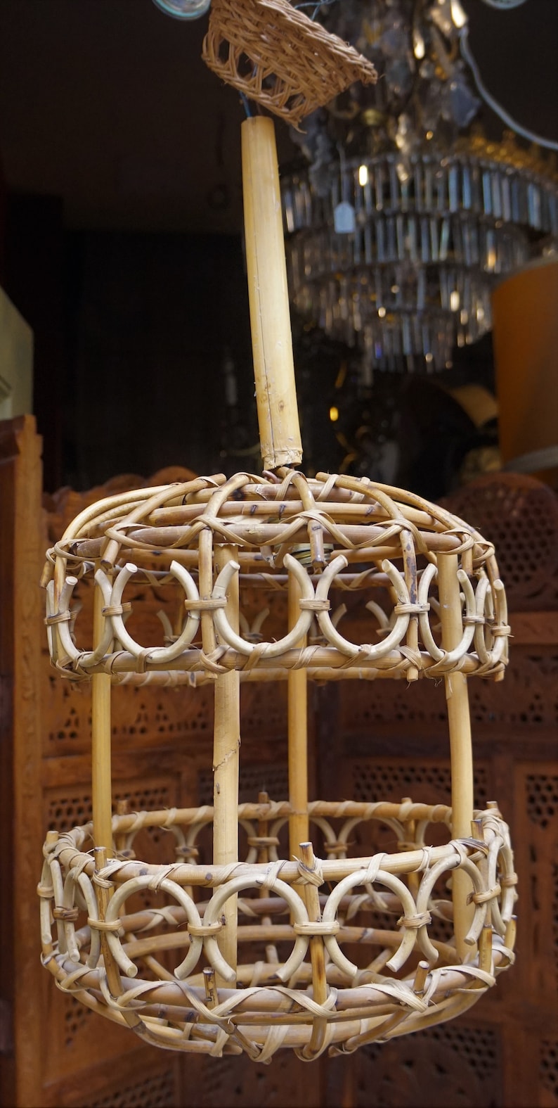 May include: A round, woven bamboo pendant light fixture with a natural brown color. The light fixture has a circular top and bottom with a woven design. The fixture is suspended from a single, thick bamboo pole.