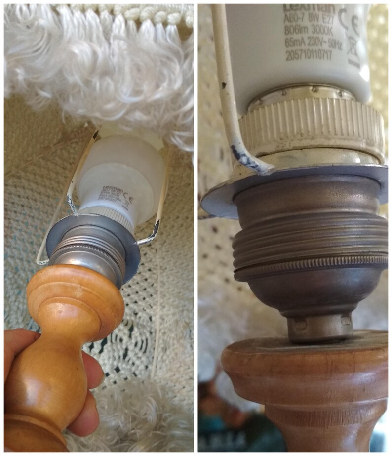 Op de afbeelding: Close-up van een lampvoet met een witte lampenkap en een gloeilamp. De lampvoet is gemaakt van hout en heeft een metalen fitting. De lampenkap is gemaakt van witte stof met een franje.