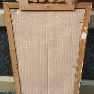 May include: A vintage wooden picture frame with a gold-painted finish. The frame has a decorative top with a carved design. The back of the frame is made of cardboard.