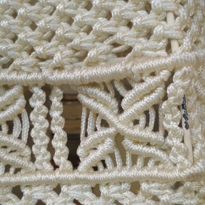 Op de afbeelding: Close-up van een witte macram&eacute; wandhanger met een geometrisch patroon. De macram&eacute; is gemaakt van dik, wit koord en heeft een geweven textuur.