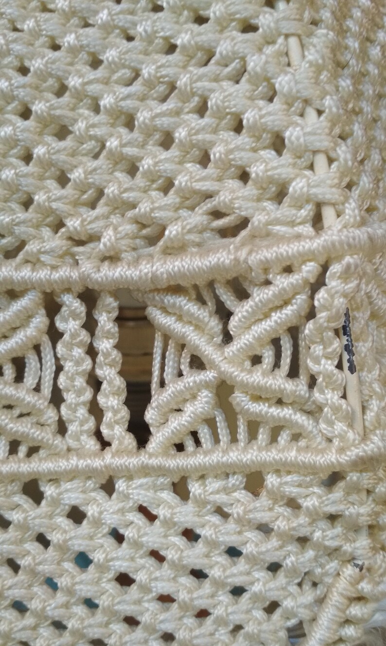 Op de afbeelding: Close-up van een witte macram&eacute; wandhanger met een geometrisch patroon. De macram&eacute; is gemaakt van dik, wit koord en heeft een geweven textuur.