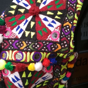 May include: A colorful embroidered fabric with a geometric pattern and small mirrors. The fabric is decorated with pom-poms in various colors.