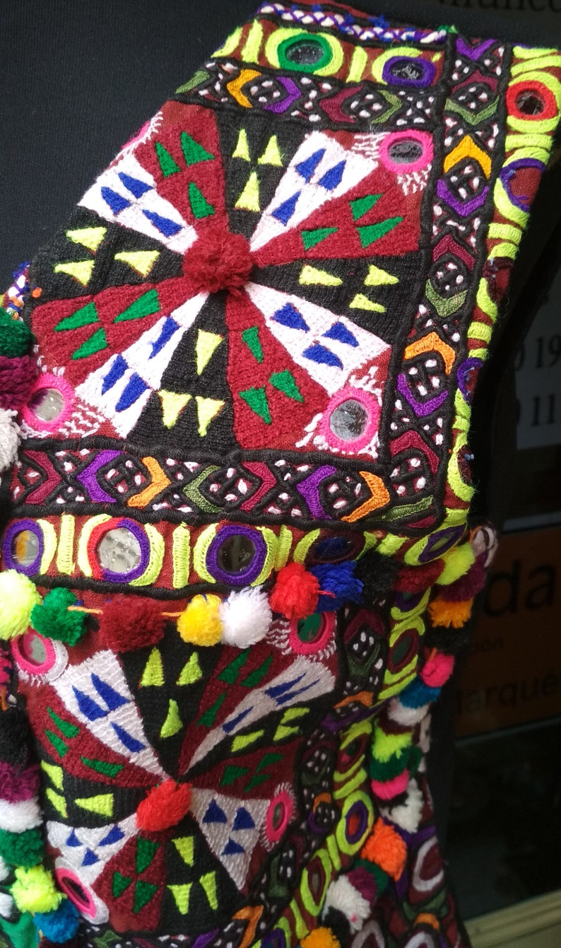 May include: A colorful embroidered fabric with a geometric pattern and small mirrors. The fabric is decorated with pom-poms in various colors.