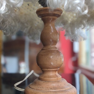 Op de afbeelding: Een houten lampenvoet met een witte, pluche lampenkap. De voet heeft een bolle vorm met een afgeronde bovenkant en een brede basis.